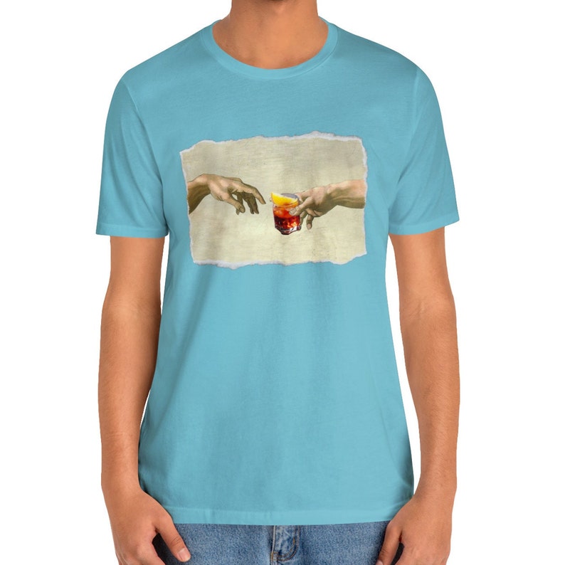 May include: A light blue t-shirt with a graphic of two hands reaching towards each other, holding a glass of red liquid with a lemon wedge. The graphic is a parody of the famous "The Creation of Adam" painting.