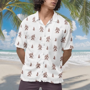 May include: A white short-sleeved button-down shirt with a brown and white pattern of Bigfoot and pine trees.