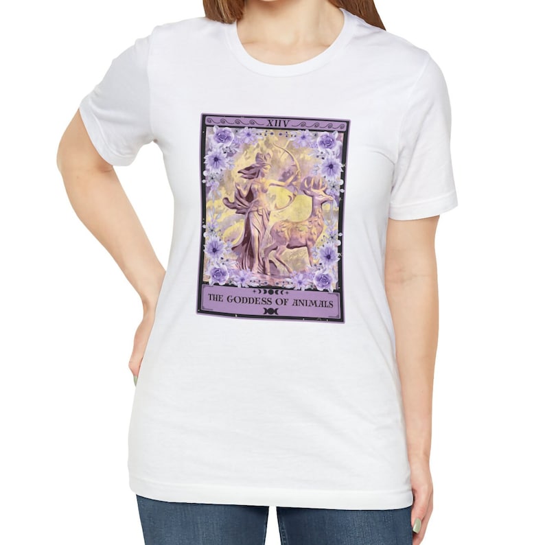 May include: White t-shirt with a purple and white tarot card design. The card depicts a woman with a bow and arrow standing next to a deer. The card reads "XIV THE GODDESS OF ANIMALS".