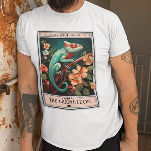 May include: White t-shirt with a graphic of a chameleon on a branch with flowers. The graphic is in a card-like frame with the text "XVII THE CHAMELEON" at the bottom.