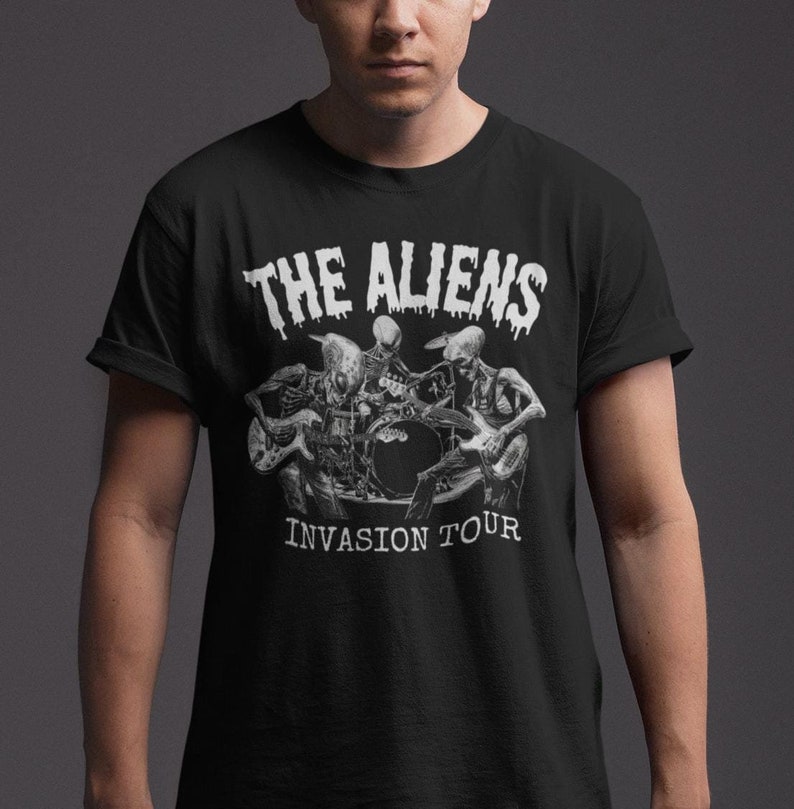 Puede incluir: Camiseta negra con un gr&aacute;fico blanco de tres esqueletos alien&iacute;genas tocando instrumentos. El texto "THE ALIENS INVASION TOUR" est&aacute; impreso debajo del gr&aacute;fico.