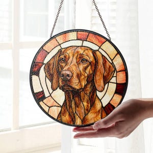 Könnte beinhalten: Runde Glasmalerei mit einem Vizsla-Hund. Das Design hat einen schwarzen Rand und einen Mosaikhintergrund in Braun-, Orange- und Cremetönen. Das Fell des Hundes ist detailliert in Brauntönen dargestellt, mit einer Kette zum Aufhängen. Durchmesser ca. 20 cm.