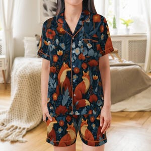 Puede incluir: Un conjunto de pijama de dos piezas con un estampado floral azul oscuro con zorros y flores naranjas. La parte superior de manga corta y los pantalones cortos tienen ribetes naranjas. El pijama est&aacute; hecho de un material suave y c&oacute;modo.