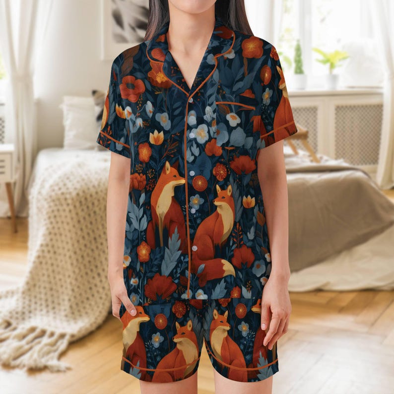 Puede incluir: Un conjunto de pijama de dos piezas con un estampado floral azul oscuro con zorros y flores naranjas. La parte superior de manga corta y los pantalones cortos tienen ribetes naranjas. El pijama est&aacute; hecho de un material suave y c&oacute;modo.