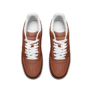 May include: A pair of brown leather low-top sneakers with white laces and a white sole. The sneakers have a small white logo on the side that says "BXC".