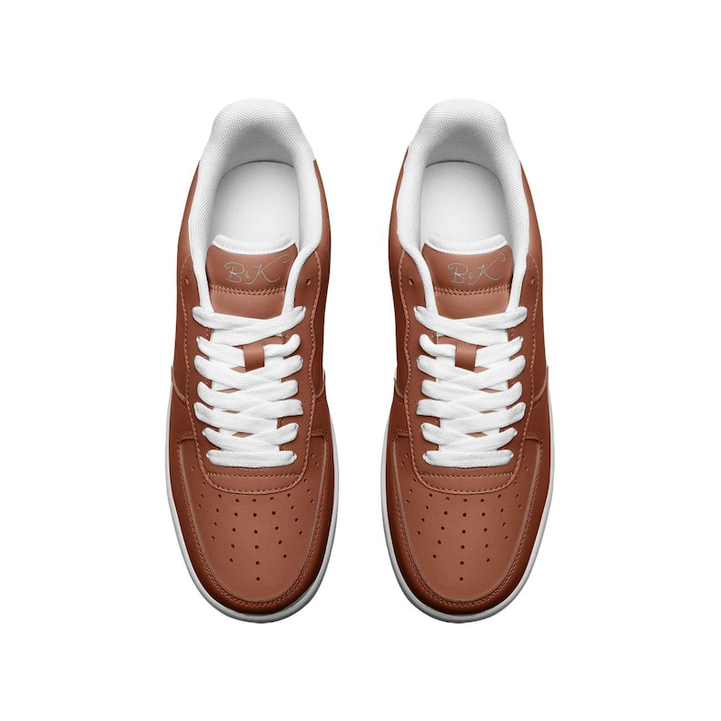 May include: A pair of brown leather low-top sneakers with white laces and a white sole. The sneakers have a small white logo on the side that says "BXC".