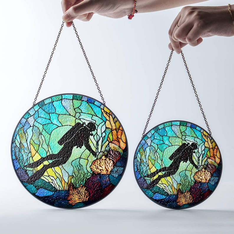 Op de afbeelding: Twee gebrandschilderde raamhangers met een duiker in een blauwe, groene en gele onderwater sc&egrave;ne. De grotere hanger heeft een diameter van 30 cm en de kleinere een diameter van 20 cm.