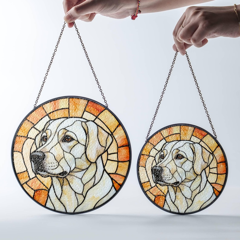 May include: Two round stained glass dog portraits, featuring a Labrador Retriever. The artwork has a black border and a chain for hanging. The background is a mosaic of orange and yellow hues, with the dog's face in shades of white and cream.