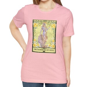 May include: Pink t-shirt with a graphic of a tarot card depicting a woman with flowers and the text "XIV THE GODDESS OF LOVE"