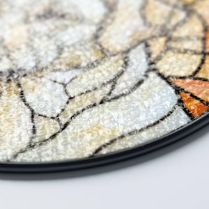 May include: Close-up of a decorative, round object with a mosaic-like design. The design features a mix of white, beige, and orange segments, outlined with black lines. The object has a black border and a textured surface.