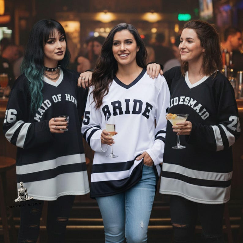 Pu&ograve; includere: Tre persone indossano maglie in stile hockey bianche e nere. La persona al centro indossa una maglia bianca con la scritta "BRIDE" sul davanti. Le altre due indossano maglie nere con "MAID OF HONOR" e "BRIDESMAID". Ogni maglia ha un numero sulla manica.