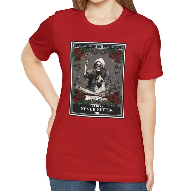 Pu&ograve; includere: Maglietta rossa con un design di carta dei tarocchi che presenta uno scheletro in una tunica con cappuccio che tiene una coppa. La carta dice "XVII NEVER BETTER".