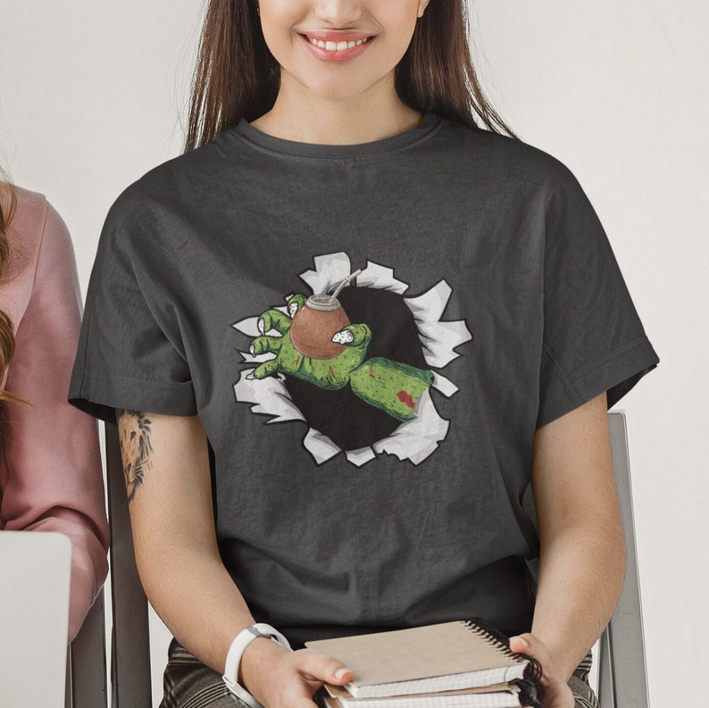 May include: A dark gray t-shirt with a graphic of a green zombie hand reaching out of a ripped hole, holding a brown and green mate gourd.