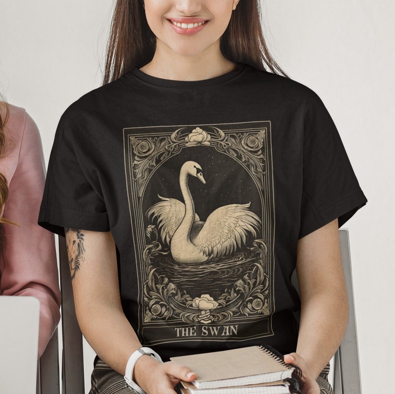 May include: Black t-shirt with a vintage illustration of a swan in a decorative frame. The text "THE SWAN" is printed below the image.