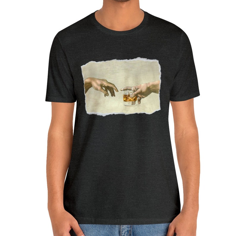 K&ouml;nnte beinhalten: Ein schwarzes T-Shirt mit einem Vintage-Bild von zwei H&auml;nden, die sich gegenseitig erreichen, wobei eine ein Glas mit bernsteinfarbener Fl&uuml;ssigkeit h&auml;lt. Das Bild ist mit einem zerrissenen Papierrahmen versehen.