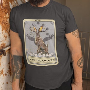 May include: A dark gray t-shirt with a vintage tarot card design featuring a jackalope with antlers and a crescent moon. The card is labeled "XXVII THE JACKALOPE".