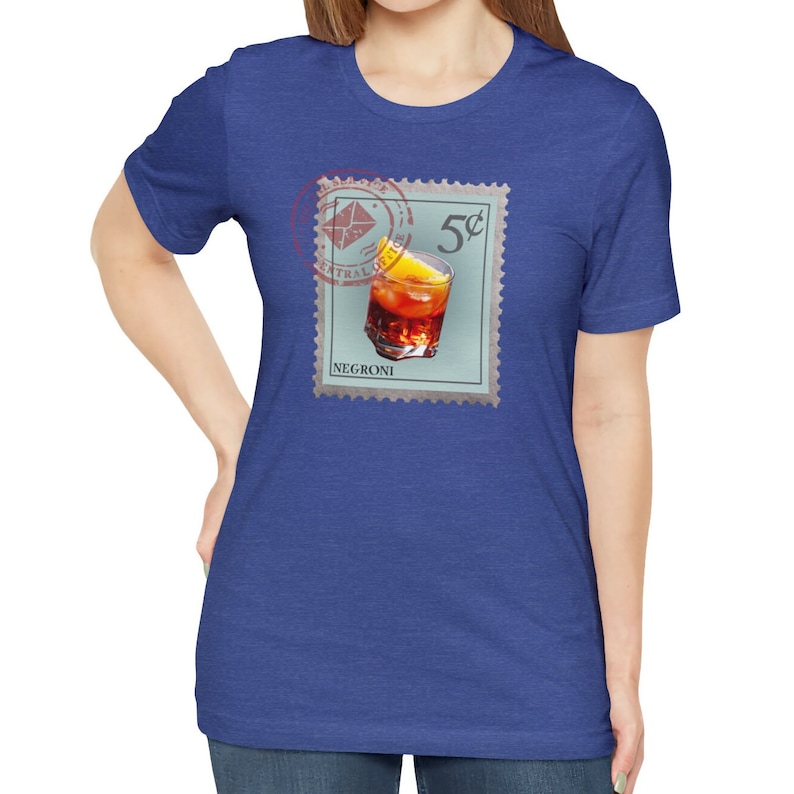 May include: A blue t-shirt with a vintage-style stamp featuring a glass of Negroni with an orange slice. The stamp reads "5&cent;" and "NEGRONI".
