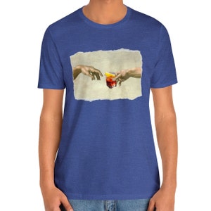 May include: A blue t-shirt with a graphic of two hands reaching towards each other, holding a glass of red liquid with a lemon wedge. The graphic is in a distressed, ripped paper style.
