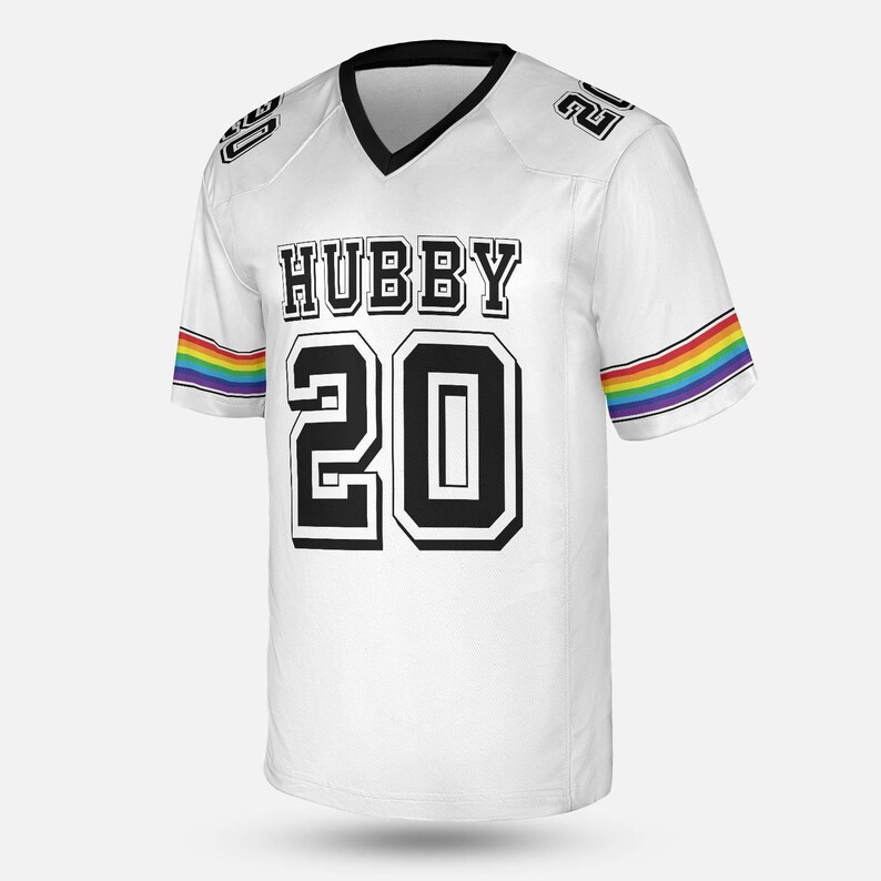 Puede incluir: Camiseta de f&uacute;tbol blanca con ribete negro y cuello en V. La camiseta presenta la palabra "HUBBY" sobre el n&uacute;mero "20" en negro. Rayas arco&iacute;ris adornan las mangas. El n&uacute;mero "20" tambi&eacute;n est&aacute; en los hombros.