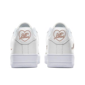 May include: A pair of white leather sneakers with a rose gold heart and "Just Married" text on the back of each shoe.