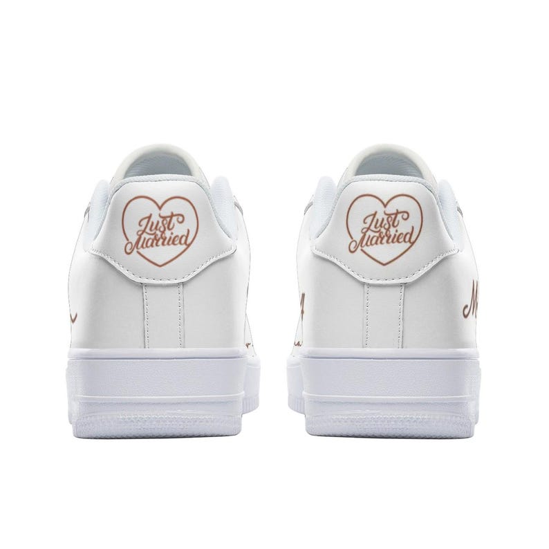 May include: A pair of white leather sneakers with a rose gold heart and "Just Married" text on the back of each shoe.