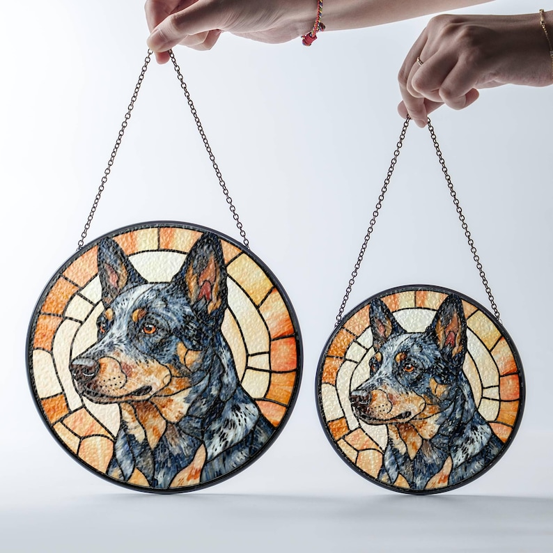May include: Two round stained glass dog portraits, each with a black metal frame and chain for hanging. The dog is a blue heeler with a detailed, colorful design. The background is a warm, orange and yellow pattern.