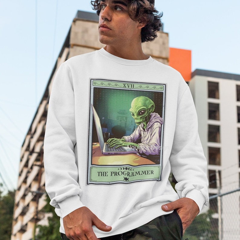 Peut inclure: Sweat-shirt blanc avec un extraterrestre vert portant un sweat &agrave; capuche et tapant sur un ordinateur portable. L'image est dans un style de carte de tarot avec le texte "XVIII THE PROGRAMMER" en bas.