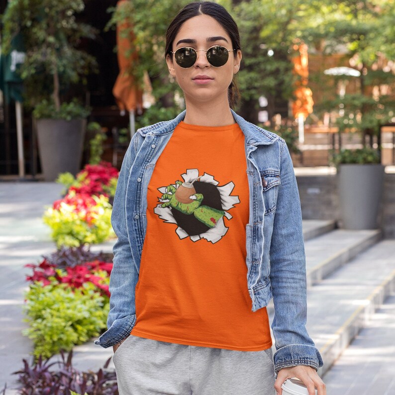 May include: Orange t-shirt with a graphic of a zombie hand reaching out of a ripped hole. The hand is green and holding a glass of liquid.