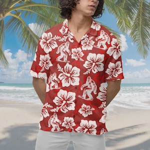 May include: A red short-sleeved button-down shirt with a white hibiscus flower and white silhouette of a Bigfoot surfing pattern.