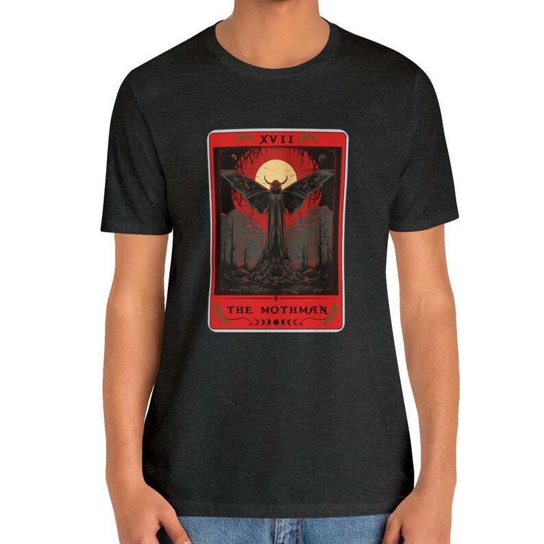 May include: A dark heather grey t-shirt featuring a red and black tarot card design. The card depicts a black mothman with large wings, a red moon, and the text "XVII THE MOTHMAN".