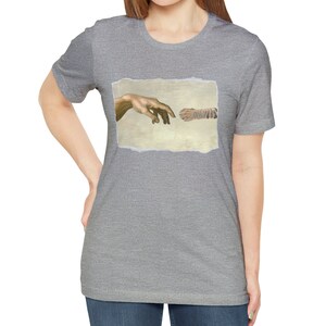 May include: A gray t-shirt with a graphic of a cat paw and a human hand reaching out to touch it, inspired by the famous painting "The Creation of Adam".
