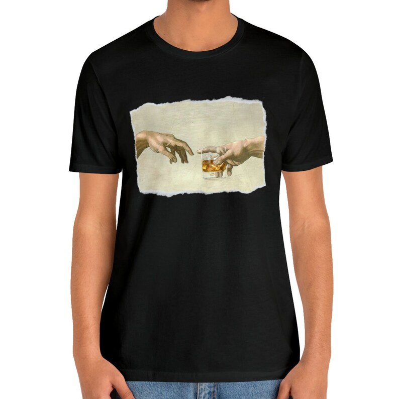 K&ouml;nnte beinhalten: Ein schwarzes T-Shirt mit einem Aufdruck von zwei H&auml;nden, die sich gegenseitig erreichen, wobei eine ein Glas Whisky h&auml;lt. Der Druck befindet sich auf einem strukturierten, beigefarbenen Hintergrund.