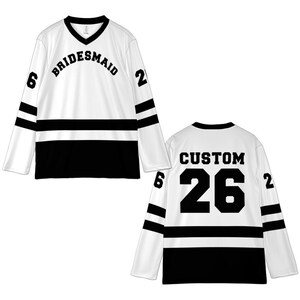 Pu&ograve; includere: Maglia da hockey bianca e nera con la scritta "BRIDESMAID" sul petto. La maglia ha strisce nere sulle maniche e una fascia nera nella sezione centrale. Il retro della maglia dice "CUSTOM 26".