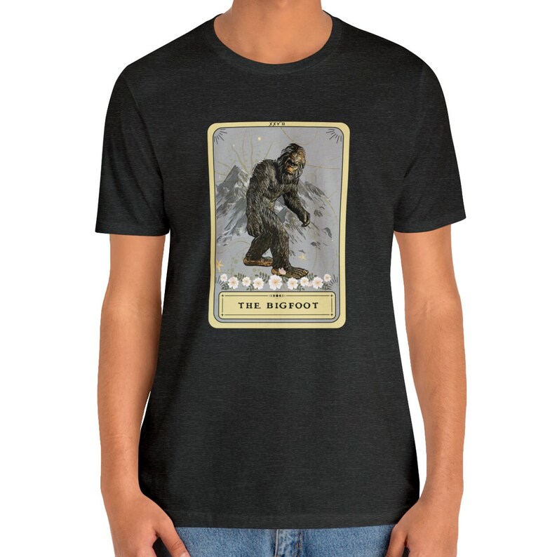 Pode incluir: Uma camiseta cinza escura mesclada com uma ilustra&ccedil;&atilde;o vintage de Bigfoot em um cart&atilde;o com o texto "THE BIGFOOT".