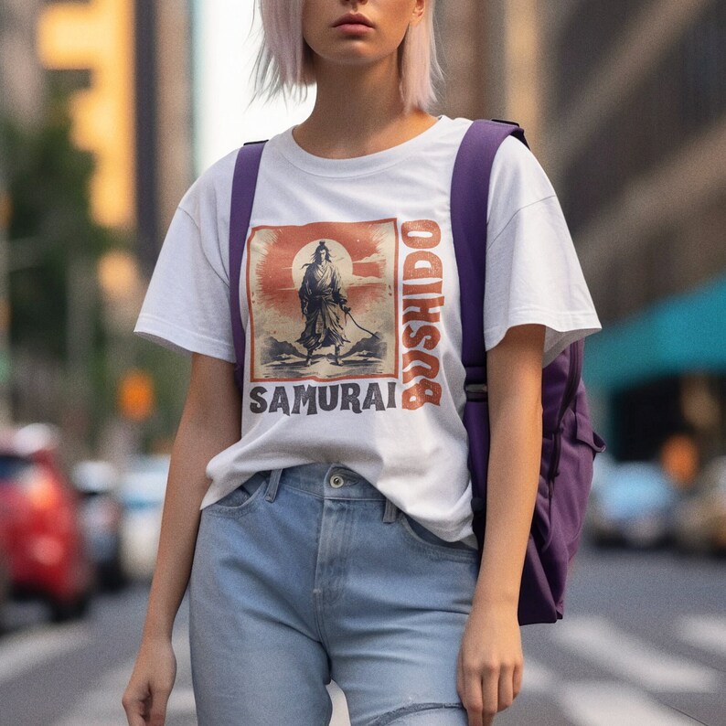 May include: White t-shirt featuring a vintage-style graphic of a samurai warrior with the text "BUSHIDO" and "SAMURAI" in orange and black. The design includes a red sun and a warrior holding a sword. The shirt is paired with light blue jeans.