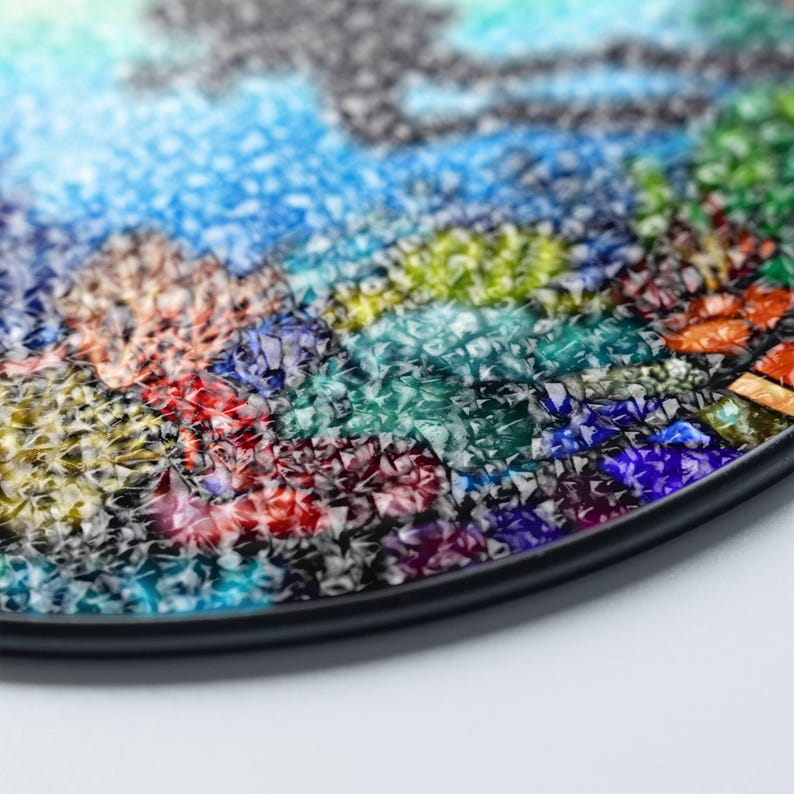 Op de afbeelding: Een ronde, kleurrijke moza&iuml;ekbak met een zwarte rand. De moza&iuml;ek is gemaakt van kleine, onregelmatige stukjes glas in tinten blauw, groen, rood, oranje en geel.