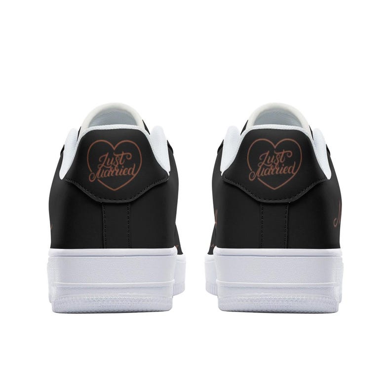 May include: A pair of black sneakers with white soles. The back of each shoe has a heart with the text "Just Married" in a copper color.