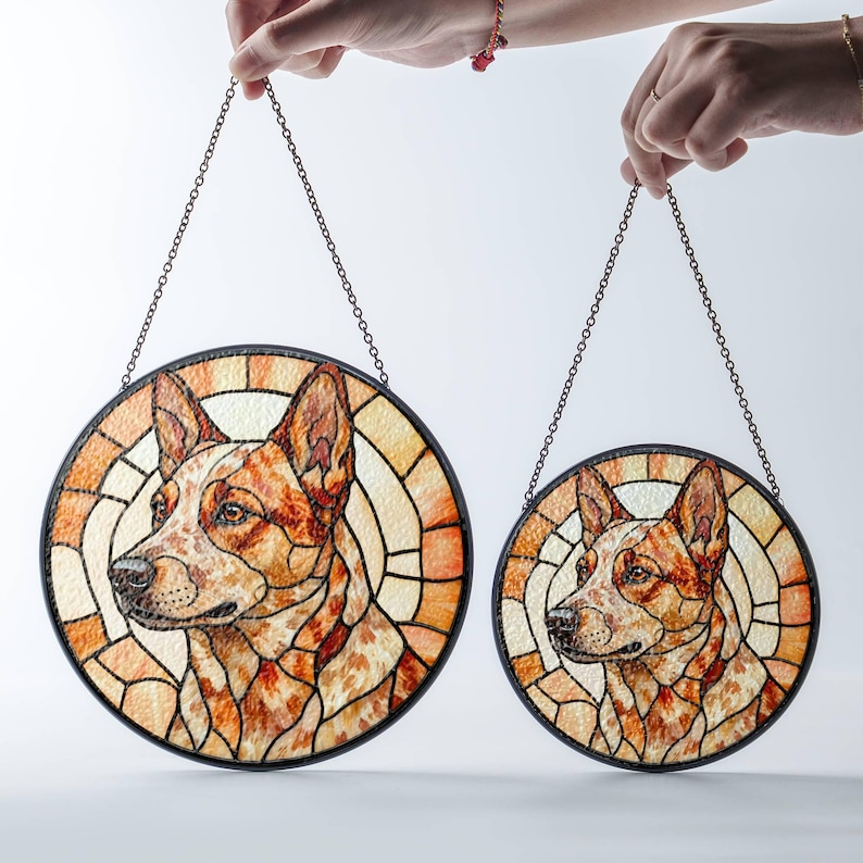 May include: Two round stained glass dog portraits, one large and one small, are suspended by chains. The dog portraits feature a red and white dog breed with a black border and a stained glass background in shades of orange and cream.