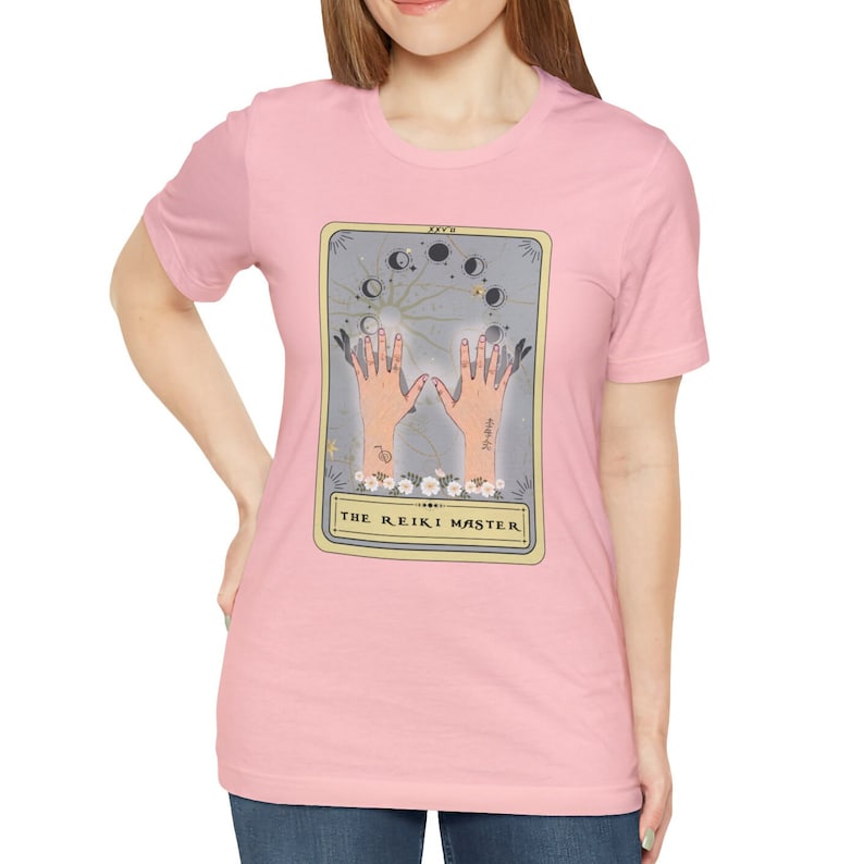 May include: Pink t-shirt featuring a tarot card graphic with a hand gesture and the text "The Reiki Master".