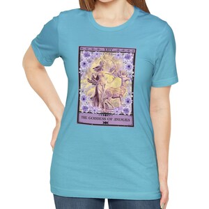 May include: A light blue t-shirt with a tarot card design featuring a purple goddess figure with a bow and arrow, a deer, and floral accents. The card reads "XIV. THE GODDESS OF ANIMALS".