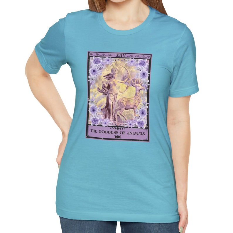 May include: A light blue t-shirt with a tarot card design featuring a purple goddess figure with a bow and arrow, a deer, and floral accents. The card reads "XIV. THE GODDESS OF ANIMALS".