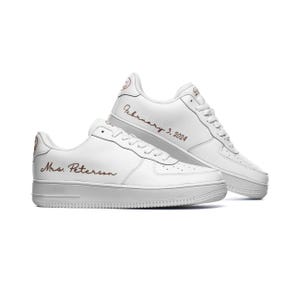 May include: A pair of white leather sneakers with a brown inscription. The inscription on the left shoe reads "Mrs. Peterson" and the inscription on the right shoe reads "February 3, 2024".