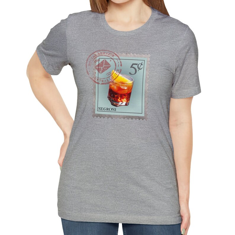 May include: A gray t-shirt with a vintage-style postage stamp design featuring a Negroni cocktail. The stamp reads "Postal Service Central Office 5&cent; Negroni".