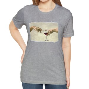 May include: A heather grey t-shirt with a graphic of two hands reaching towards a glass of red wine. The graphic is a parody of the famous "The Creation of Adam" painting.