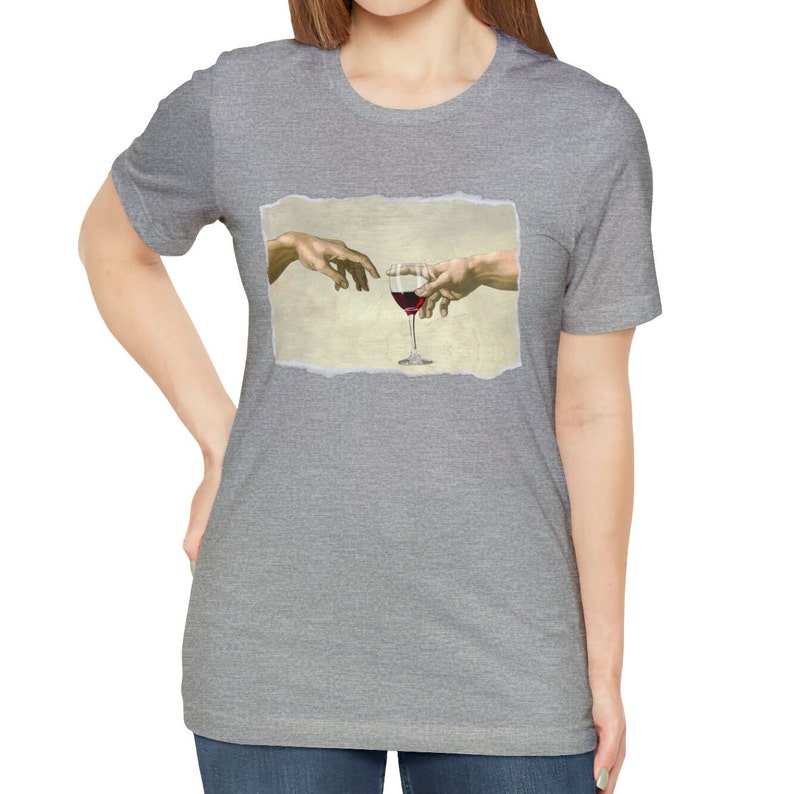 May include: A heather grey t-shirt with a graphic of two hands reaching towards a glass of red wine. The graphic is a parody of the famous "The Creation of Adam" painting.
