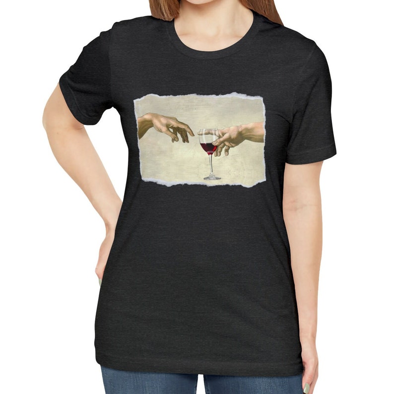 May include: A black t-shirt with a white, ripped-paper frame featuring a painting of two hands reaching towards a glass of red wine.