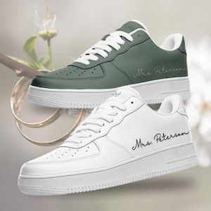 May include: Two pairs of white sneakers with a personalized inscription. One pair is white with black lettering that says "Mrs. Peterson". The other pair is green with white lettering that says "Mrs. Peterson".