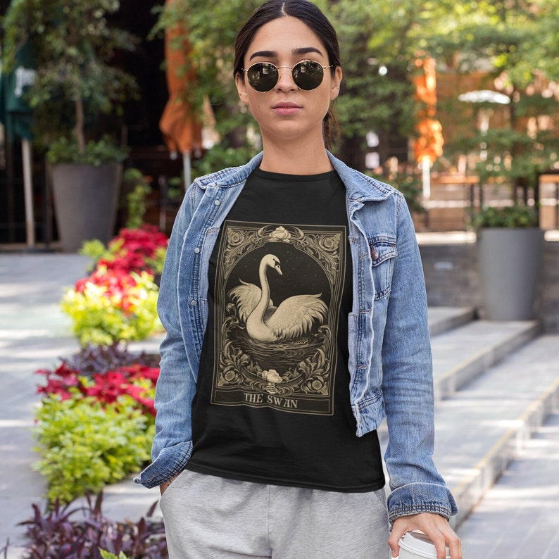 May include: A black t-shirt with a vintage illustration of a swan in a frame. The text "THE SWAN" is printed below the image.