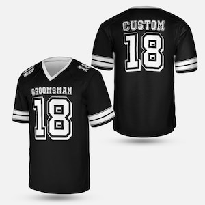 May include: Black football jersey with white accents, featuring the word "GROOMSMAN" above the number "18" on the front. The back of the jersey displays "CUSTOM" above the number "18". The jersey has white stripes on the sleeves.