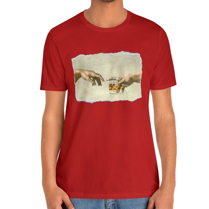 K&ouml;nnte beinhalten: Ein rotes T-Shirt mit einem wei&szlig;en, zerrissenen Rechteck, das ein Gem&auml;lde von zwei H&auml;nden zeigt, die sich gegenseitig erreichen, wobei eine ein Glas mit bernsteinfarbener Fl&uuml;ssigkeit h&auml;lt. Das Gem&auml;lde ist eine Parodie auf Michelangelos "Die Erschaffung Adams".